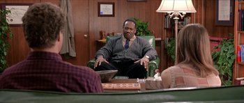 Movie still from “Old School” (2003), directed by Todd Phillips – A man sitting in a chair in front of a table; Medium shot, Over the shoulder angle