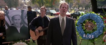 Movie still from “Old School” (2003), directed by Todd Phillips – A man in a suit and tie singing and a man playing a guitar; Medium shot, Over the shoulder angle