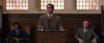 Movie still from “Old School” (2003), directed by Todd Phillips – A man standing at a podium in front of a glass of water; Medium shot, Low angle