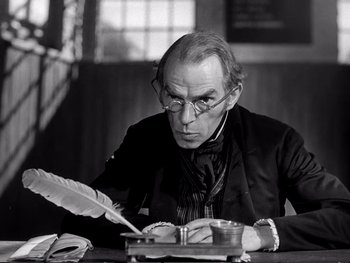 Movie still from “Oliver Twist” (1948), directed by David Lean – An older man writing on a paper with a quill pen; Close Up shot, Low angle