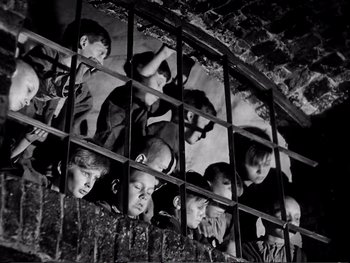 Movie still from “Oliver Twist” (1948), directed by David Lean – A group of young boys looking through bars of a jail cell; Medium shot, High angle