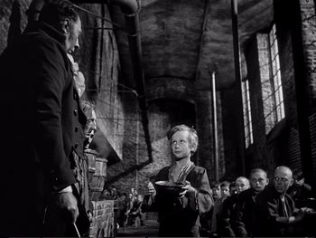 Movie still from “Oliver Twist” (1948), directed by David Lean – An old photo of a woman holding a plate in front of an old man; Medium shot, Low angle