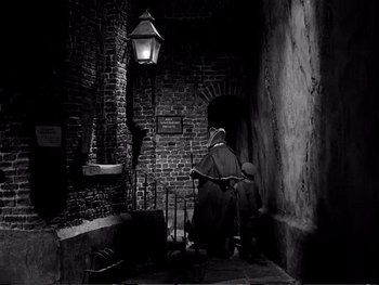 Movie still from “Oliver Twist” (1948), directed by David Lean – An old woman sitting on a chair under a street light; Wide shot, High angle