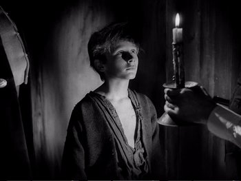 Movie still from “Oliver Twist” (1948), directed by David Lean – A young man holding a candle in a dark room; Medium shot, Over the shoulder angle