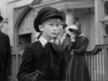 Movie still from “Oliver Twist” (1948), directed by David Lean – A young boy wearing a hat and holding a cane; Medium shot, High angle
