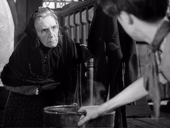 Movie still from “Oliver Twist” (1948), directed by David Lean – An old woman looking at a man cooking food; Medium shot, Over the shoulder angle