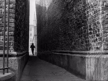 Movie still from “Oliver Twist” (1948), directed by David Lean – A person is walking down a narrow alley way; Extreme Wide shot, High angle
