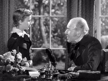 Movie still from “Oliver Twist” (1948), directed by David Lean – An older man and a young woman are sitting at a table; Medium shot, Over the shoulder angle