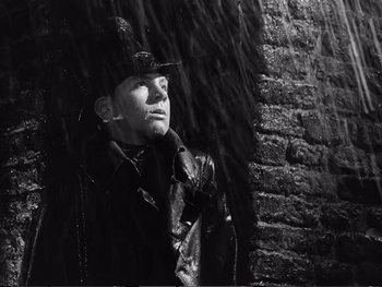 Movie still from “Oliver Twist” (1948), directed by David Lean – A man in a leather jacket and hat standing in front of a brick wall; Close Up shot, Low angle