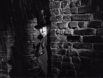 Movie still from “Oliver Twist” (1948), directed by David Lean – A man wearing a top hat standing next to a brick wall; Medium shot, Low angle