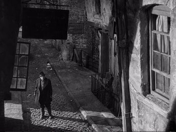 Movie still from “Oliver Twist” (1948), directed by David Lean – An old man walking down the street holding a bag; Wide shot, High angle