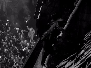 Movie still from “Oliver Twist” (1948), directed by David Lean – A man standing on top of a building next to a crowd of onlookers; Wide shot, Overhead angle
