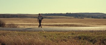 Movie still from “On the Road” (2012), directed by Walter Salles – A man walking down a road near a grassy field; Wide shot, Over the shoulder angle