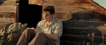 Movie still from “On the Road” (2012), directed by Walter Salles – A man sitting on the ground looking at his cell phone; Medium shot, Low angle