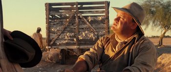 Movie still from “On the Road” (2012), directed by Walter Salles – A man in a hat sitting in front of a wooden crate; Close Up shot, Over the shoulder angle
