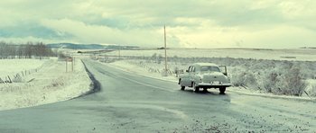Movie still from “On the Road” (2012), directed by Walter Salles – A car is driving down the road on a cloudy day; Extreme Wide shot, High angle