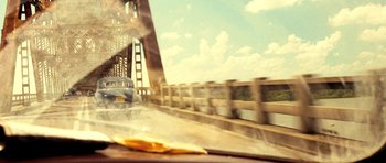 Movie still from “On the Road” (2012), directed by Walter Salles – A car driving on a bridge over a body of water; Wide shot, Over the shoulder angle