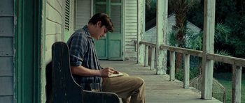 Movie still from “On the Road” (2012), directed by Walter Salles – A man sitting on a chair on a porch looking at his phone; Medium shot, Low angle