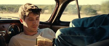 Movie still from “On the Road” (2012), directed by Walter Salles – A man sitting in the back seat of a car reading a book; Close Up shot, Over the shoulder angle