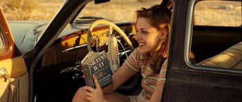 Movie still from “On the Road” (2012), directed by Walter Salles – A woman sitting in the drivers seat of a car holding a book; Medium shot, High angle