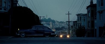 Cars driving down a street at night with a city in the background