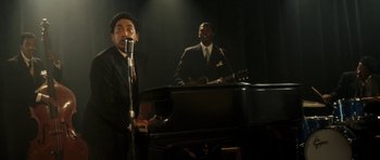 Movie still from “On the Road” (2012), directed by Walter Salles – Two men in suits are singing in front of a piano; Medium shot, Low angle