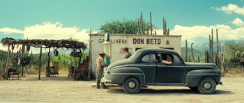Movie still from “On the Road” (2012), directed by Walter Salles – An old car parked in front of a building; Wide shot, Over the shoulder angle