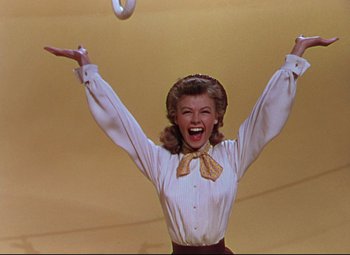 Movie still from “On the Town” (1949), directed by Gene Kelly – A woman in white shirt and brown skirt holding a frisbee; Medium shot, Low angle