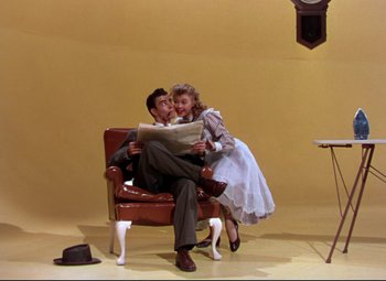 Movie still from “On the Town” (1949), directed by Gene Kelly – A man and a woman sitting in a chair reading a newspaper; Wide shot, High angle