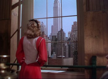 Movie still from “On the Town” (1949), directed by Gene Kelly – A woman standing in front of an open window looking at a skyscraper; Wide shot, Low angle