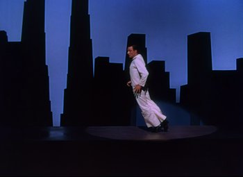Movie still from “On the Town” (1949), directed by Gene Kelly – A man walking on a stage in front of buildings; Wide shot, Low angle