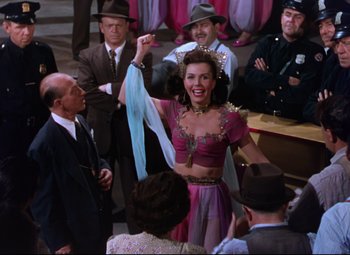 Movie still from “On the Town” (1949), directed by Gene Kelly – A woman in a pink and purple dress is holding a blue scarf; Medium shot, High angle
