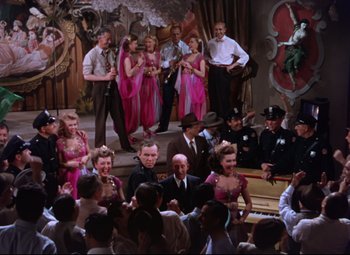 Movie still from “On the Town” (1949), directed by Gene Kelly – A group of people standing in a room with a piano; Wide shot, High angle