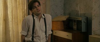 Movie still from “One Day” (2011), directed by Lone Scherfig – A young man wearing suspenders in a room with floral wallpaper; Medium shot, Over the shoulder angle