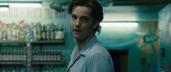 Movie still from “One Day” (2011), directed by Lone Scherfig – A man with long brown hair standing in front of a bar; Close Up shot, Over the shoulder angle
