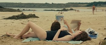 Movie still from “One Day” (2011), directed by Lone Scherfig – A man and a woman laying on the beach reading; Medium shot, High angle
