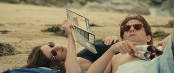 Movie still from “One Day” (2011), directed by Lone Scherfig – A man and a woman laying on the beach reading a magazine; Medium shot, Over the shoulder angle