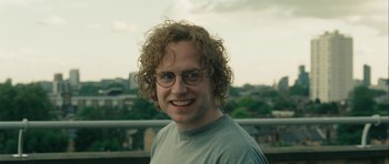 Movie still from “One Day” (2011), directed by Lone Scherfig – A man with curly blonde hair wearing glasses; Close Up shot, Low angle