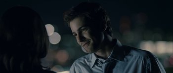 Movie still from “One Day” (2011), directed by Lone Scherfig – A young man is smiling for the camera in the dark; Close Up shot, Over the shoulder angle