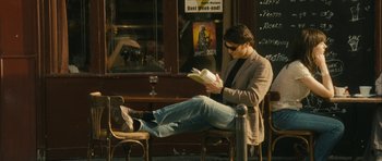 Movie still from “One Day” (2011), directed by Lone Scherfig – A man sitting on top of a chair reading a book; Wide shot, Over the shoulder angle