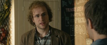 Movie still from “One Day” (2011), directed by Lone Scherfig – A man in glasses and a brown jacket is standing in a room; Close Up shot, Over the shoulder angle