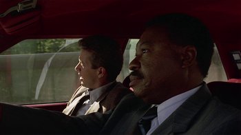 Movie still from “One False Move” (1991), directed by Carl Franklin – Two men in suits driving in a red car; Close Up shot, Over the shoulder angle