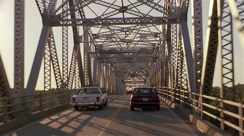 Movie still from “One False Move” (1991), directed by Carl Franklin – Two cars driving on a bridge over a river; Extreme Wide shot, Low angle