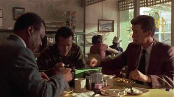 Movie still from “One False Move” (1991), directed by Carl Franklin – A group of people sitting at a table in a restaurant; Medium shot, Over the shoulder angle