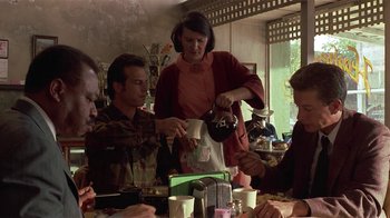 Movie still from “One False Move” (1991), directed by Carl Franklin – A group of people sitting at a table with cups of coffee; Medium shot, Over the shoulder angle