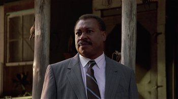 Movie still from “One False Move” (1991), directed by Carl Franklin – A man in a suit and tie standing in front of wooden posts; Close Up shot, Low angle