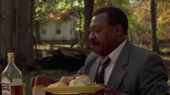 Movie still from “One False Move” (1991), directed by Carl Franklin – A man in a suit holding a tray of bread; Close Up shot, Over the shoulder angle
