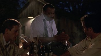 Movie still from “One False Move” (1991), directed by Carl Franklin – A man sitting at a table with a bottle of beer; Medium shot, Over the shoulder angle