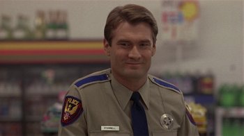 Movie still from “One False Move” (1991), directed by Carl Franklin – A man in a uniform is smiling for the camera; Close Up shot, Over the shoulder angle