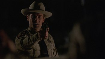 Movie still from “One False Move” (1991), directed by Carl Franklin – A man in a hat and uniform pointing a gun at the camera; Close Up shot, Over the shoulder angle